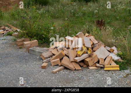 Il pelo di rottami di legno impilato in modo ordinato sul lato della strada ghiaiosa durante il giorno. Foto Stock