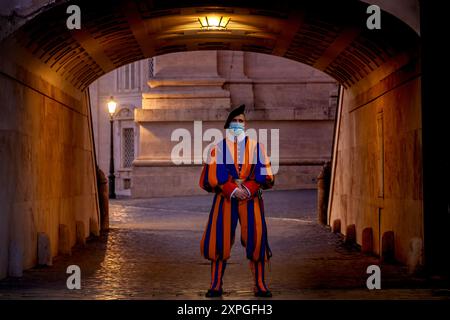 La Guardia Svizzera in uniforme tradizionale è vigile in un vicolo Vaticano, incarnando tradizione e sicurezza moderna con una maschera durante la pandemia Foto Stock