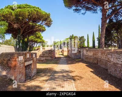 Edifici funerari di una o due piani quadrati, spesso circondati da un recinto; soffitti a botte o tetti piatti; facciate in mattoni adornate con timpani triangolari, plinti, lesbiche, colonne e capitelli; piccole finestre e porte incorniciate da soglie in travertino, stipiti ed epistoli. La necropoli si sviluppò ai lati della via Flavia tra la fine del i e il IV secolo d.C. - Necropoli di Portus nell'Isola Sacra, Fiumicino, Roma, Italia Foto Stock