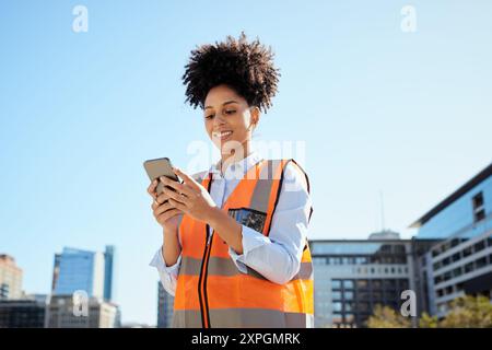 Lavoratrice edile sicura di sé che utilizza lo smartphone presso il moderno cantiere urbano Foto Stock