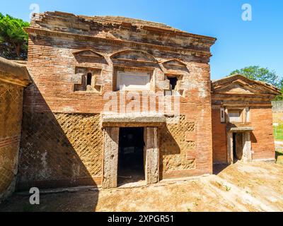 Edifici funerari di una o due piani quadrati, spesso circondati da un recinto; soffitti a botte o tetti piatti; facciate in mattoni adornate con timpani triangolari, plinti, lesbiche, colonne e capitelli; piccole finestre e porte incorniciate da soglie in travertino, stipiti ed epistoli. La necropoli si sviluppò ai lati della via Flavia tra la fine del i e il IV secolo d.C. - Necropoli di Portus nell'Isola Sacra, Fiumicino, Roma, Italia Foto Stock