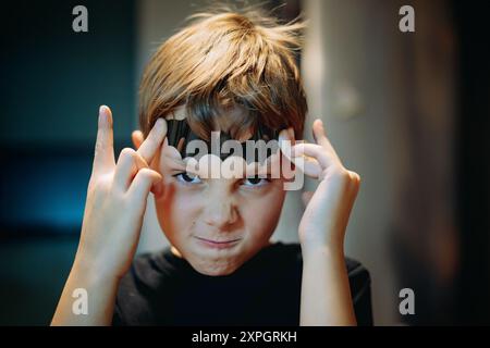 carino ragazzo caucasico che tiene una pipistrello di carta sulla fronte e fa paura al viso. Foto di alta qualità Foto Stock