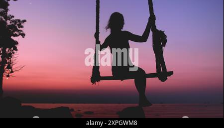 Una donna in silhouette siede su un'altalena sulla spiaggia segreta dell'isola di Koh Phangan, in Thailandia, mentre il sole tramonta sullo sfondo. Foto Stock