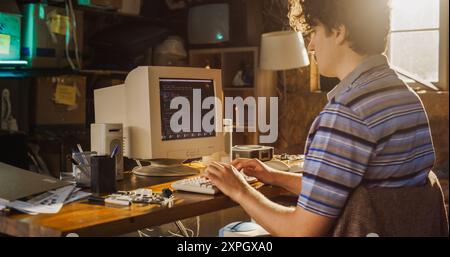 Ingegnere informatico maschio caucasico programmazione su vecchio computer desktop in retro Garage. Sviluppatore di software esperto che scrive codice per l'avvio di nuovi dispositivi portatili innovativi negli anni Novanta. Foto Stock