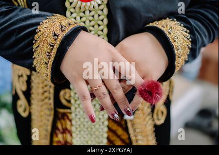 Le mani della sposa asiatica. Indossa un tipico kebaya nero indonesiano decorato con fiori di gelsomino e paes ageng giavanese Foto Stock