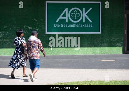 Menschen gehen vor der AOK filiale in Essen am Berliner Platz entlang, AOK-Logo, allgemein, Feature, Randmotiv, Symbolfoto Essen, 06.08.2024. *** Persone che camminano lungo Berliner Platz di fronte alla filiale AOK di Essen, logo AOK, generale, caratteristica, motivo di confine, foto simbolica Essen, 06 08 2024 Foto Stock