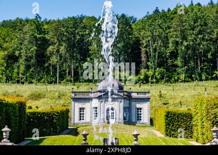 Getto d'acqua che sgorga in primo piano dalla fontana nei giardini del Castello di Freyr, edificio in stile rinascimentale sullo sfondo, alberi lussureggianti contro il cielo blu, sunn Foto Stock