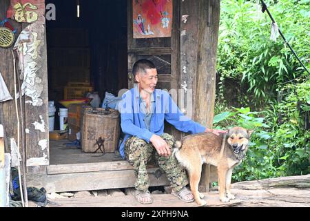 (240806) -- LONGLIN, 6 agosto 2024 (Xinhua) -- Un abitante del villaggio siede sulla soglia del suo edificio Ganlan in legno nel villaggio Pingliu della contea di Longlin nella regione autonoma di Guangxi Zhuang, nella Cina meridionale, 31 luglio 2024. Il villaggio di Pingliu, che abbraccia una storia di oltre 200 anni, è un villaggio di minoranza etnica Zhuang che confina con le province vicine dello Yunnan e Guizhou. Tra le tradizioni e i costumi ben conservati del gruppo etnico locale Zhuang, la struttura abitativa locale, l'edificio Ganlan, un'architettura residenziale strutturata in legno di palafitte, è molto caratteristico. Sostenuto da colonne in legno, t Foto Stock