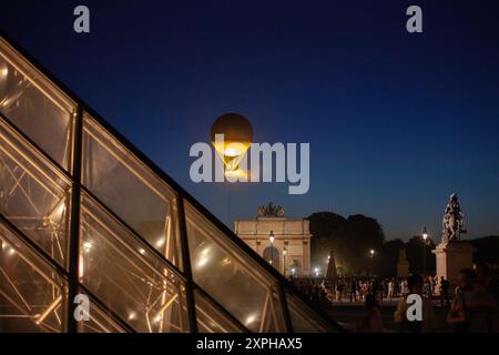 Quando il sole tramonta su Parigi, molte persone curiose vengono a riunirsi al Louvre con la Piramide per vedere il Caldrone Olimpico del 2024 Foto Stock