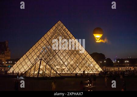 Quando il sole tramonta su Parigi, molte persone curiose vengono a riunirsi al Louvre con la Piramide per vedere il Caldrone Olimpico del 2024 Foto Stock