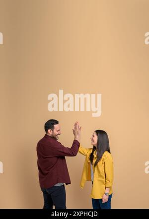 Vista laterale dell'uomo e della donna gioiosi che si danno cinque alti l'uno all'altro e gridano su sfondo beige. Coppia eccitata che batte le mani e saluta Foto Stock