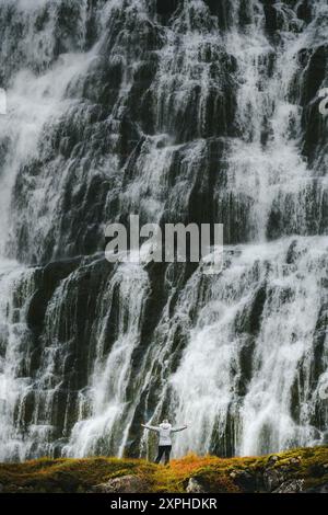 Piccolo escursionista di fronte alla massiccia cascata Dynjandi, nel Westfjords d'Islanda, godendo di una vista maestosa Foto Stock