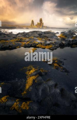 Le famose montagne basaltiche di Londrangar in Islanda in una giornata buia e lunare, riflessi in primo piano e turbolento oceano Foto Stock