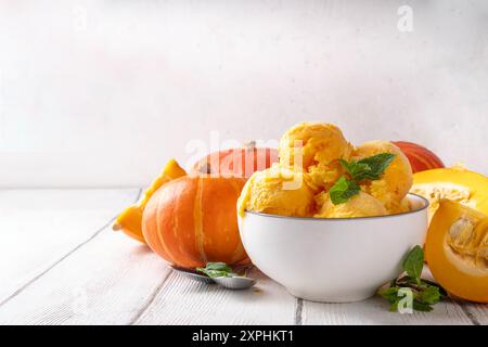 Ciotola per gelato alla zucca. Gustoso gelato con zucca in una ciotola in porzioni, su un tavolo di legno con zucca a fette, spazio per copiare Foto Stock
