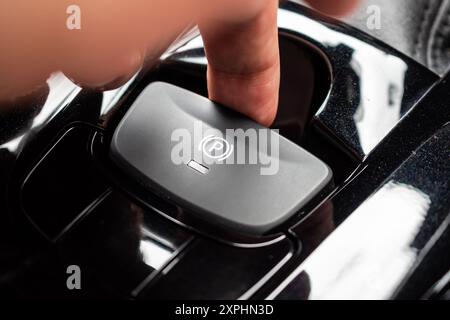 Premere a mano il pulsante del freno a mano elettronico in un'auto moderna di lusso Foto Stock