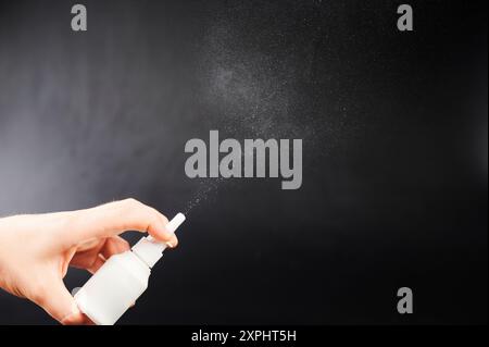 Spray nasale in mano che fuoriesce dall'ugello isolato su sfondo nero studio Foto Stock