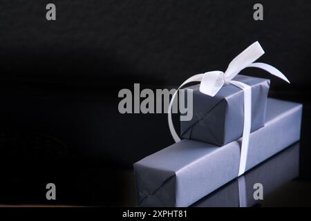 Una pila di due confezioni regalo con un nastro bianco legato intorno. Le scatole sono avvolte in carta grigia e sembrano essere un regalo per qualcuno. Concetto di Foto Stock