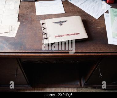 Fotografia di un libro di cimeli della seconda guerra mondiale del terzo Reich intitolato "Kriegserinnerungen" dalla Germania nazista, collocato su una scrivania di legno circondata da documenti sparsi. Rappresenta manufatti storici, memorie di guerra e storia tedesca Foto Stock