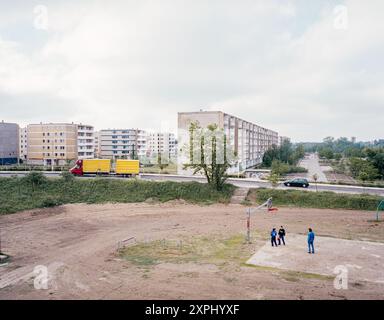 Tre bambini giocano a basket in un parco giochi polveroso circondato da appartamenti vuoti a Eisenhüttenstadt, Germania dell'Est. La scena riflette l'esodo urbano e lo svuotamento di questa città un tempo movimentata. Foto Stock