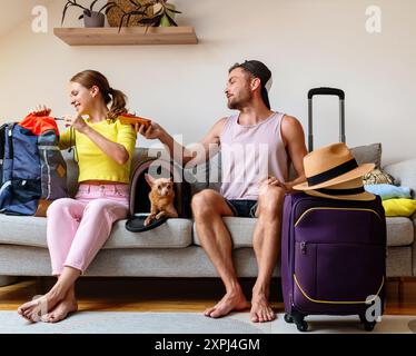 Una giovane coppia di adulti che fa il pieno di valigie da viaggio e si prepara a partire per le vacanze estive con un cane piccolo. Foto Stock