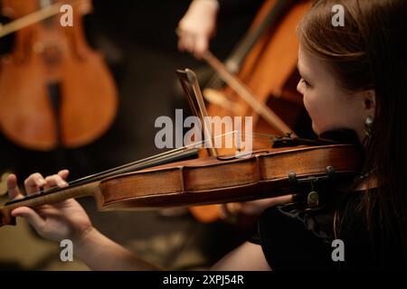 Ripresa laterale ritagliata di una musicista femminile irriconoscibile che suona violino con quartetto d'archi in studio Foto Stock