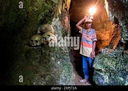 Una guida con una lanterna illumina un cranio umano in una grotta presso l'antico cimitero di Londa, il cimitero delle grotte di Toraja, Tana Toraja, Sulawesi, Indonesia Foto Stock