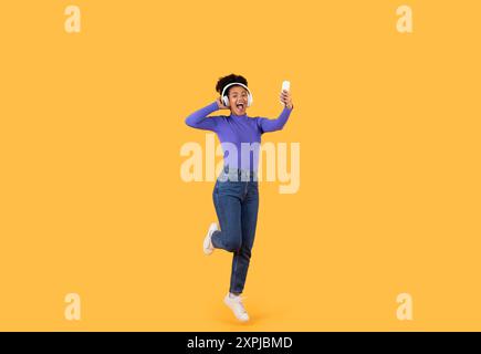 Giovane donna che danzava con gioia davanti a sfondo giallo brillante Foto Stock