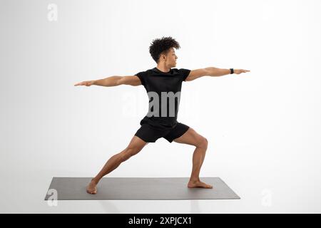 Giovane uomo che pratica la posa del guerriero nel moderno Studio durante il giorno Foto Stock