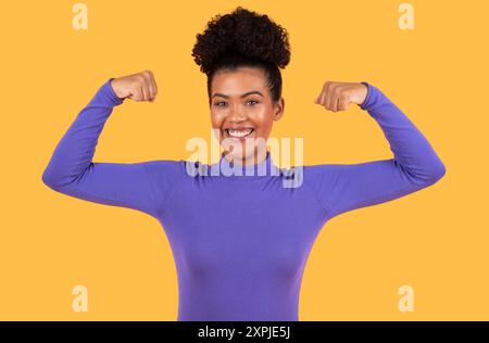 Giovane donna Flexing Muscles in Bright Purple outfit contro Yellow Foto Stock