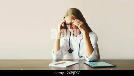 Stanca donna di mezza età medico che lavora con i documenti mentre seduto alla scrivania in ufficio di clinica medica Foto Stock