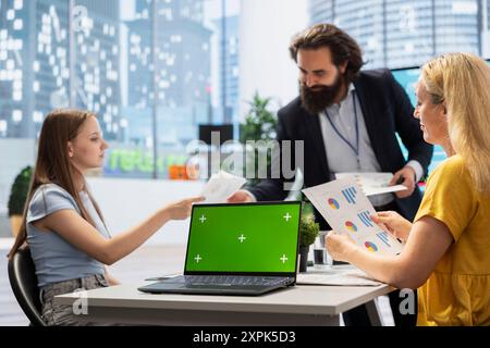 Consulente che mostra alle persone il piano finanziario su un notebook con schermo verde, aiutandole a raggiungere gli obiettivi economici. Advisor che insegna ai clienti come migliorare finanziariamente e aumentare il reddito utilizzando il notebook mockup Foto Stock