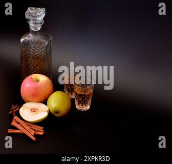 Liquore di mele con spezie su sfondo nero, alcol forte fatto in casa in un decanter di cristallo e due bicchieri, frutta matura e cannella con ani Foto Stock