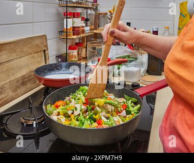 Primo piano della mano mescolando gli ingredienti in una padella con colorate verdure fritte in padella nella cucina casalinga Foto Stock