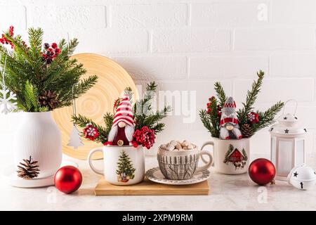 Cucina interna con piano cottura la mattina di Natale. Una tazza di cacao con marshmallow, allegri gnomi di Capodanno, palline rosse, un bouquet di rami di abete Foto Stock