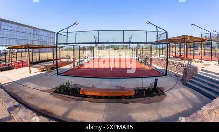 Padel Tennis su superficie rossa astro con campi recintati in vetro in campagna in una giornata di cielo blu. Foto Stock