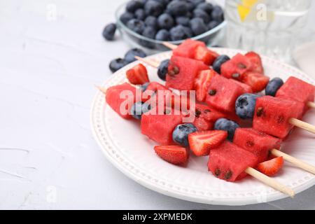 Spiedini con gustosi anguria, fragole e mirtilli su tavola bianca, primo piano Foto Stock