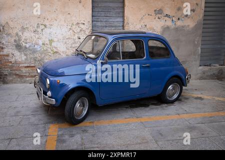 Cagliari, Italia - 22 agosto 2023: Una vecchia Fiat 500L blu 1969 parcheggiata su una strada in Italia senza persone. Vista laterale dell'auto d'epoca con un vecchio wal Foto Stock