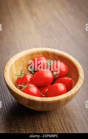 Pomodori ciliegini rossi nel recipiente su un tavolo di legno. Foto Stock