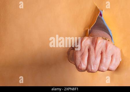 Mani di una donna anziana che puzza attraverso un buco in un giornale. Primo piano Foto Stock