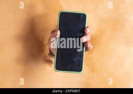 Primo piano di una donna che tiene il telefono cellulare attraverso un muro di carta strappato. smartphone con schermo vuoto Foto Stock