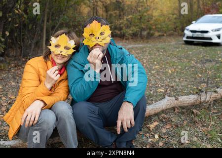 Ciao, Autunno. foto d'atmosfera stagionale. un uomo e una donna sono seduti nella foresta, coprendo i loro volti con maschere scolpite dalle foglie autunnali. rom Foto Stock