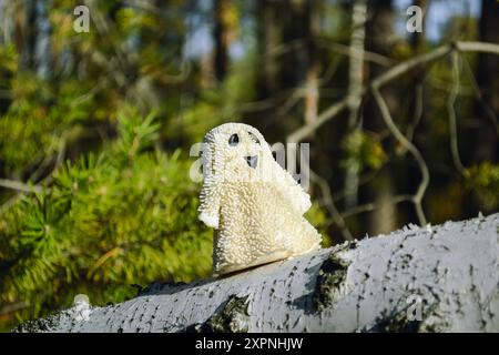 Un giocattolo fantasma sorridente si erge su una corteccia di betulla nella foresta e illuminato dal sole Foto Stock