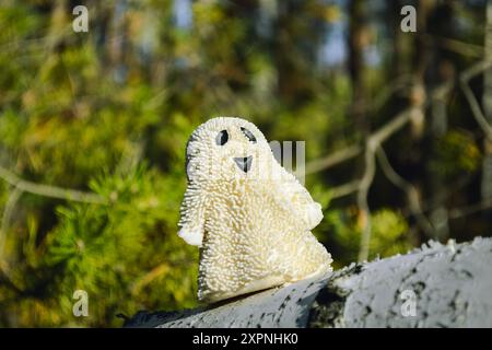 Un giocattolo fantasma sorridente si erge su una corteccia di betulla nella foresta e illuminato dal sole Foto Stock