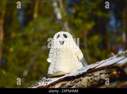 Un giocattolo fantasma sorridente si erge su una corteccia di betulla nella foresta e illuminato dal sole Foto Stock