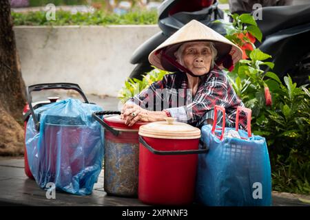 Donne che vendono frutta e verdura al mercato del cibo di strada della città vecchia di Hoi An Vietnam. Vecchia vietnamita che lavora sodo nella conica tradizionale Foto Stock