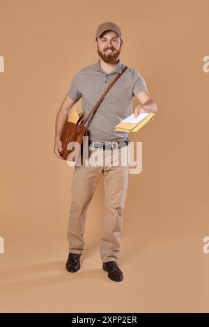 Felice giovane postino con borsa in pelle che consegna lettere su sfondo marrone Foto Stock