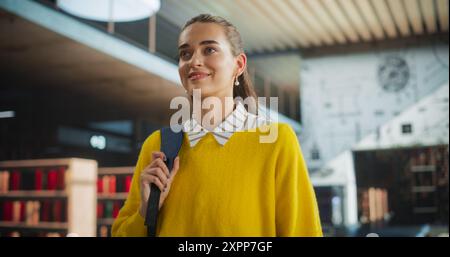 Ritratto di una giovane donna attraente che cammina all'interno di un edificio della biblioteca con uno zaino. College per le donne multietniche, edificio per uffici, centro commerciale con libreria Foto Stock