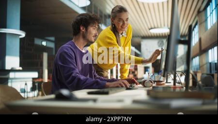 Due giovani studenti che studiano in una biblioteca universitaria. Donna che aiuta il suo compagno di classe collega maschile con i compiti. Coppia che utilizza un computer desktop per un progetto di ricerca accademica di gruppo Foto Stock