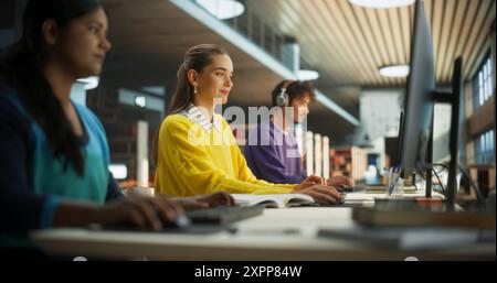 Gruppo di diversi studenti delle scuole superiori che studiano individualmente in una biblioteca pubblica. I giovani che lavorano dietro i computer, leggono libri di testo, prendono appunti nei notebook, scrivono saggi e preparano le lezioni Foto Stock