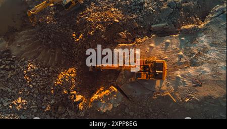 Un drone aereo è stato girato direttamente sopra l'escavatore industriale scavando le rocce sul cantiere il giorno della domenica. Lavoratori che utilizzano macchinari per completare un progetto immobiliare o estrarre risorse naturali Foto Stock